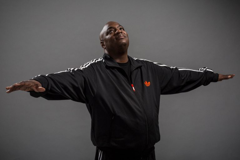 a Black man in a tracktop with his arms spread out